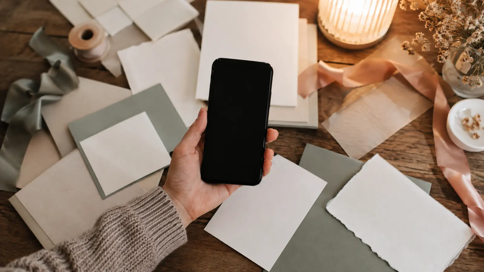 A phone held in one hand above a desk scattered with wedding stationery samples